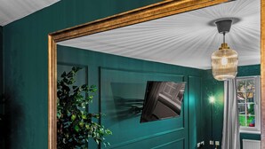 A teal-walled room with a large mirror, a hanging light fixture, and a window with a view of the outside. - Whitley Rise, Reading (Berkshire)