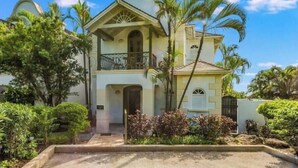 Une maison à deux étages dotée d’un balcon, entourée d’une végétation tropicale.