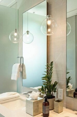 Une salle de bain moderne avec un grand miroir, un porte-serviettes, un lavabo et une plante en pot.
