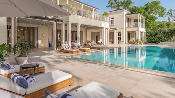 Un espace aménagé au bord de la piscine, avec des chaises longues et des parasols, une grande piscine et un bâtiment à deux étages doté de balcons.