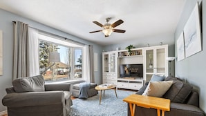 A modern living room with a grey sofa, a wooden coffee table, and a TV on a white cabinet.