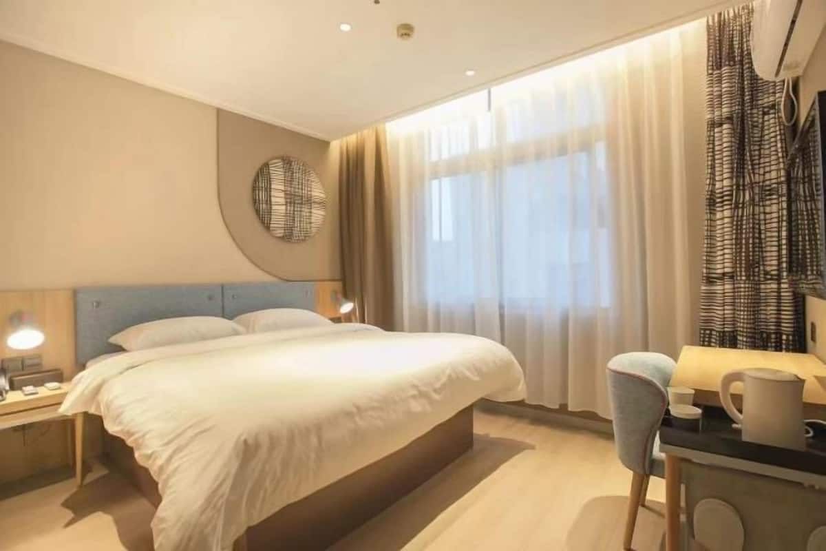 Una habitació d'hotel amb un llit, taules de nit, escriptori, cadira i una finestra amb cortines.