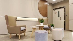 Un área de espera moderna con un sillón color beige, una pequeña mesa redonda con una planta y un reposapiés redondo.