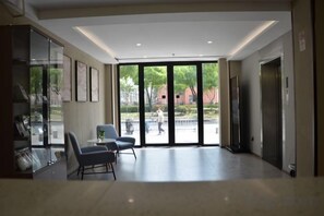 En rummelig lobby med siddeområde, en reception og en stor glasdør, der fører udendørs.