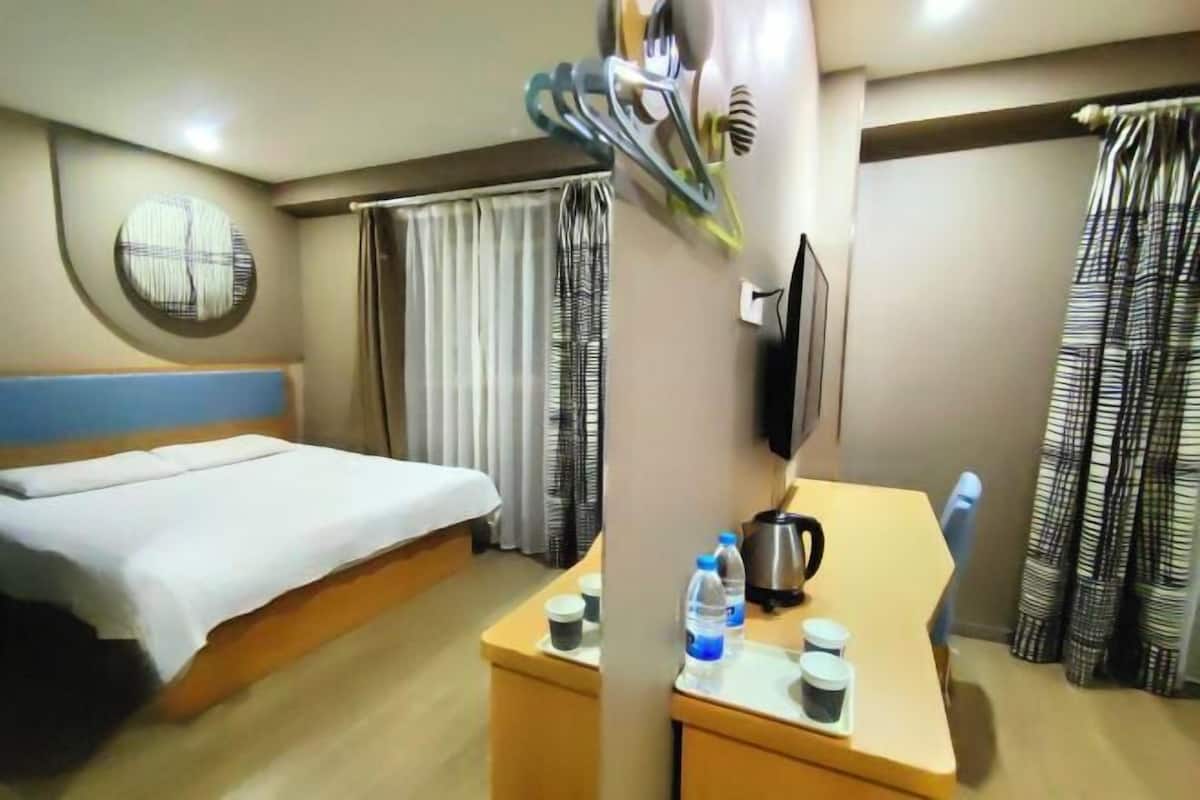 Habitació d'hotel amb llit, escriptori amb tetera, ampolles d'aigua i televisió.