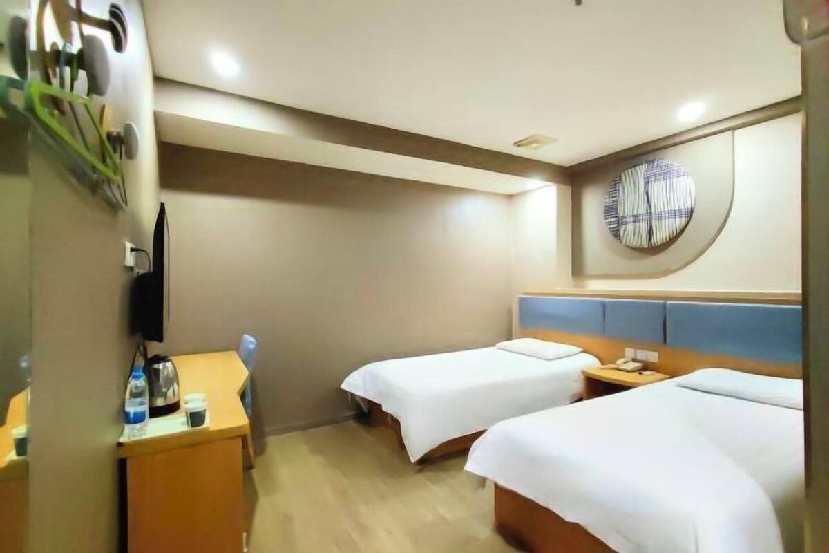 Una habitació d'hotel amb dos llits, un escriptori amb un bullidor i un televisor penjat a la paret.