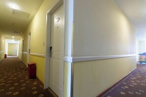 A hotel corridor with carpeted flooring, a door, and a trash bin. - Huayi Collection Hotel (Shanghai Jiuting Subway Station Jiudu Road) (Shanghai)