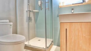 Un baño con ducha envuelta en vidrio, inodoro y tocador de madera con espejo.