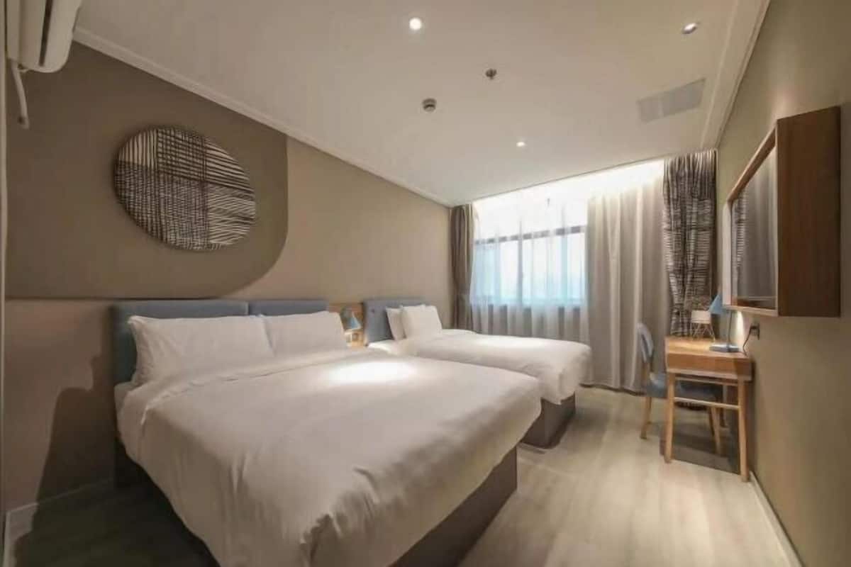 Habitació d'hotel amb dos llits, escriptori, cadira, decoració circular a la paret i finestra amb cortines.