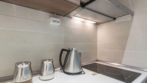 Une cuisine avec un plan de travail blanc, une bouilloire en acier inoxydable et une machine à café.