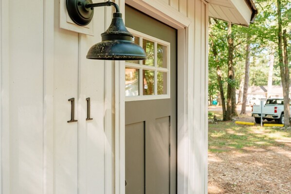 A white building with a door and a window, a black lamp, and a vehicle in the background. - Arbutus l King Suite l Sauna l SUP & Kayak Rentals (Traverse City)