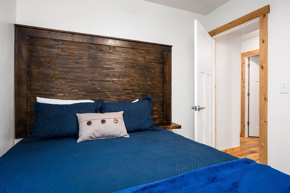 Un dormitorio con cabecera de madera, cama con ropa de cama azul y una puerta que da a otra habitación.