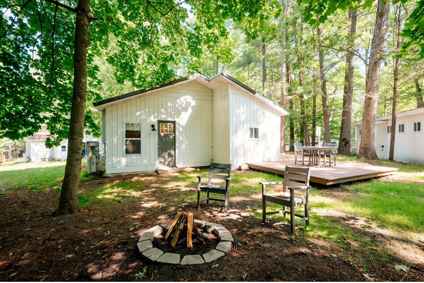 A small cabin with a deck and a fire pit in the yard.