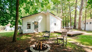 A small cabin with a deck and a fire pit in the yard.