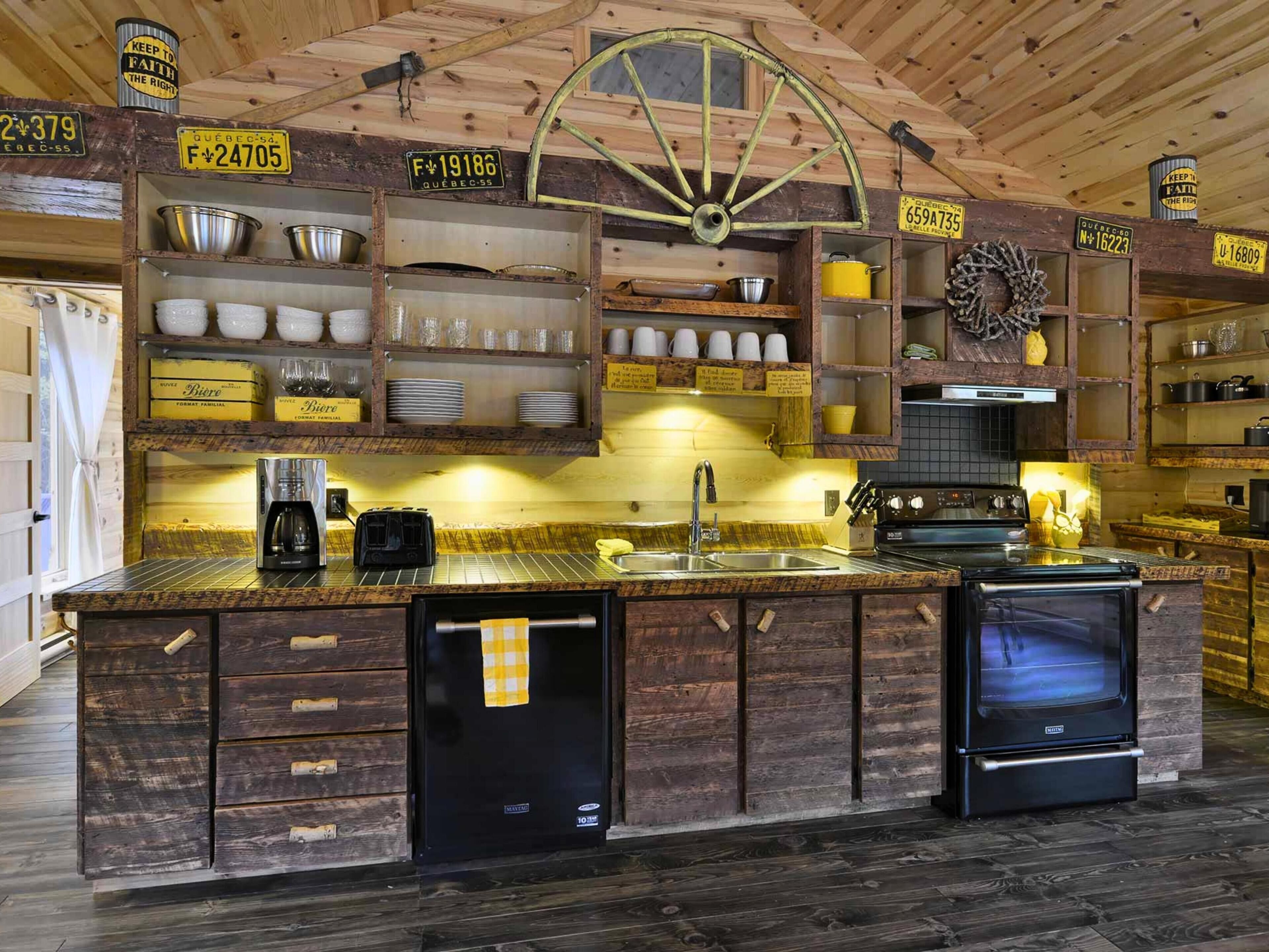 Una cocina rústica con armarios de madera, un refrigerador negro, una estufa y diversos utensilios de cocina.