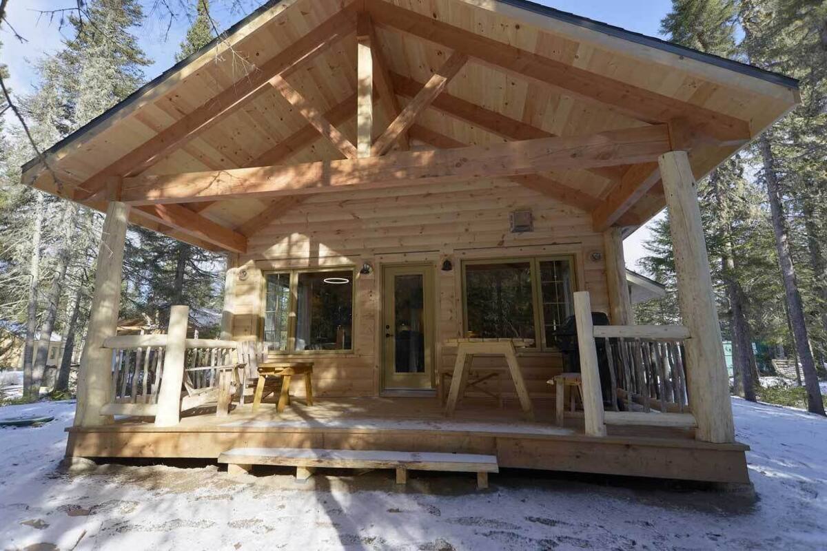 Une cabane en bois dotée d’une véranda, de grandes fenêtres et d’une porte.