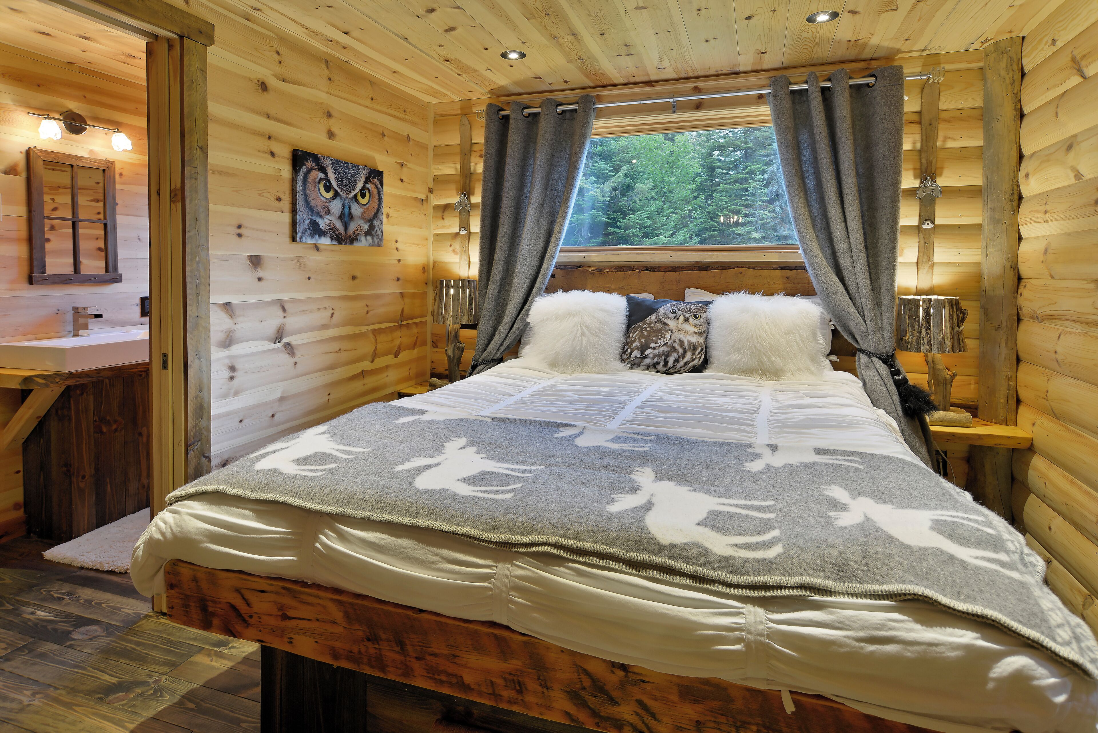 Een houten slaapkamer met een bed, gordijnen, een raam en een schilderij van een uil.