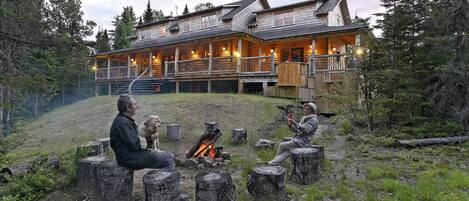 Un chalet avec un foyer au premier plan, entouré de souches d’arbres.