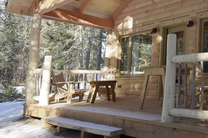 A wooden cabin with a porch, wooden chairs, and a bench.
