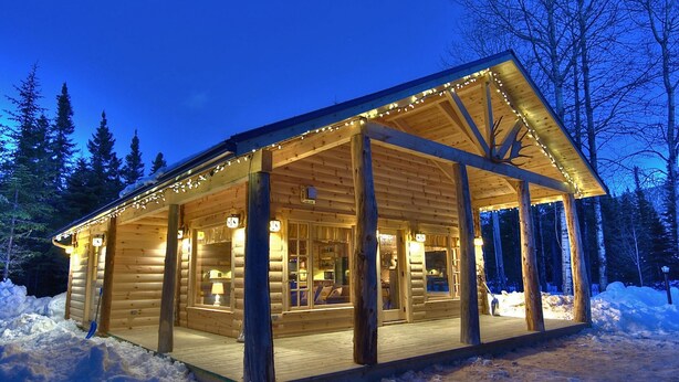 A log cabin with a covered porch and large windows, surrounded by snow. - Les Chalets de Môh  (La Malbaie)