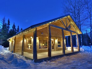 Une cabane en rondins dotée d’un porche abrité et de grandes fenêtres, entourée de neige.