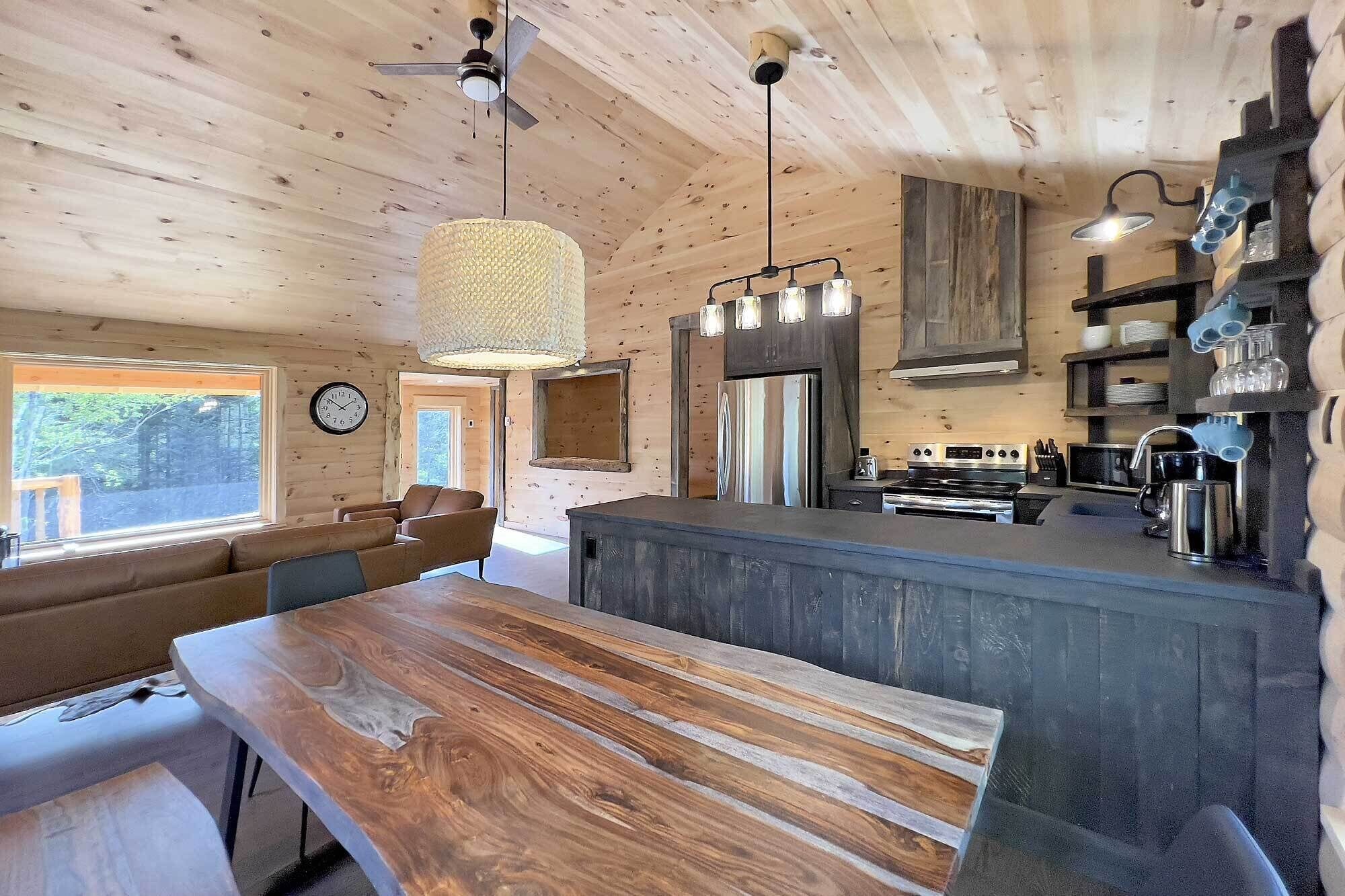 A rustic wooden interior with a dining area, kitchen, and a large window.