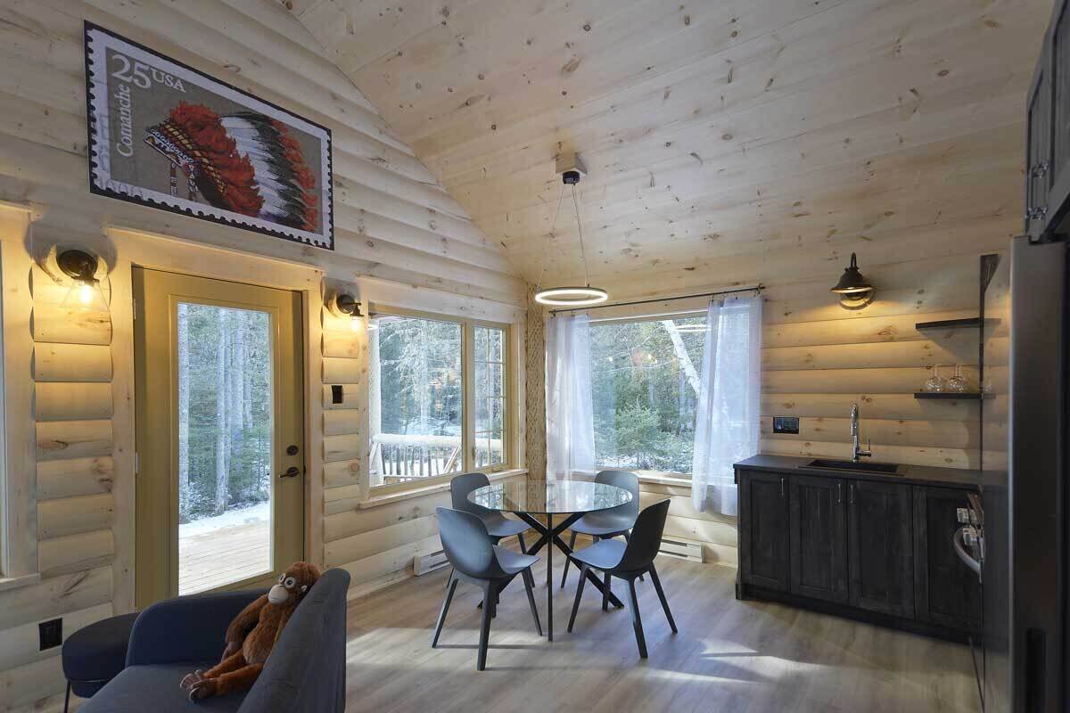 L’intérieur chaleureux d’un chalet comprend une table de salle à manger ronde, des chaises, un canapé et un coin cuisine.