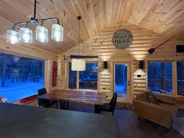 A cozy log cabin interior with a dining table, chairs, a sofa, and a sign reading "WOLF'S HEAD".