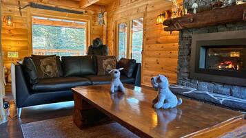 L’intérieur d’un chalet accueillant, avec une cheminée, des murs en bois, un canapé en cuir et une table basse sur laquelle sont posés des animaux en peluche.
