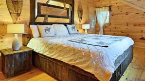 A cozy log cabin bedroom with a large bed, wooden headboard, and two bedside tables with lamps. - Les Chalets de Môh  (La Malbaie)