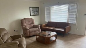 Een woonkamer met een beige bank, een relaxfauteuil en een glazen salontafel.