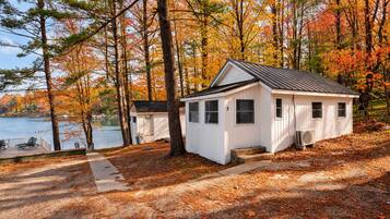 Une cabane avec un quai, entourée d’arbres aux feuilles d’automne, située près d’une étendue d’eau.