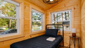 Une pièce de style cabane en bois, avec un lit, deux fenêtres et une lampe.