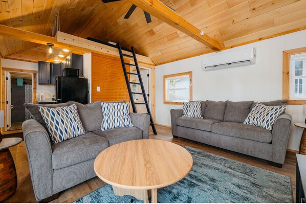 Ein gemütliches Wohnzimmer mit zwei grauen Sofas, einem Holztisch und einem blauen Teppich mit Muster.