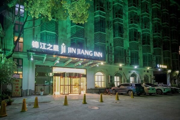 A hotel entrance with a sign reading 'JIN JIANG INN,' a gated driveway, and parked cars.