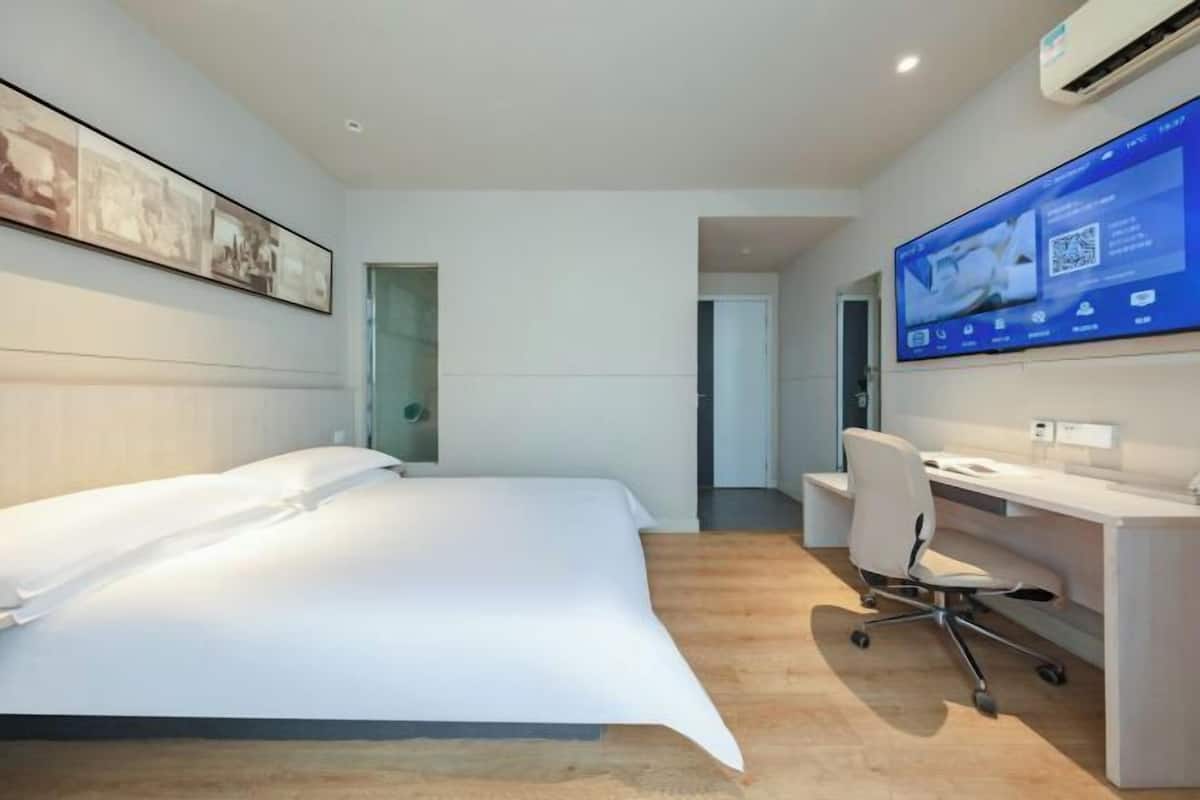 A modern hotel room with a bed, desk, and a large digital display on the wall.