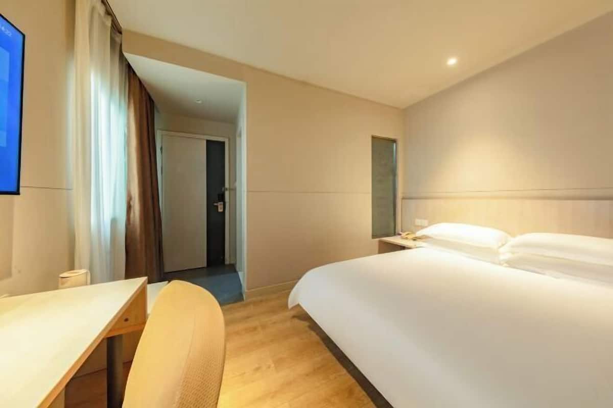A hotel room with a bed, a desk, a chair, a TV, and a door leading to another room.