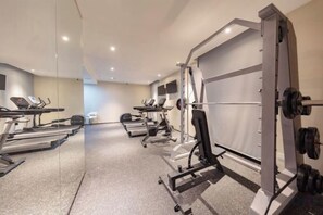 Un gimnasio con cintas de correr, máquinas de pesas y un espejo grande.