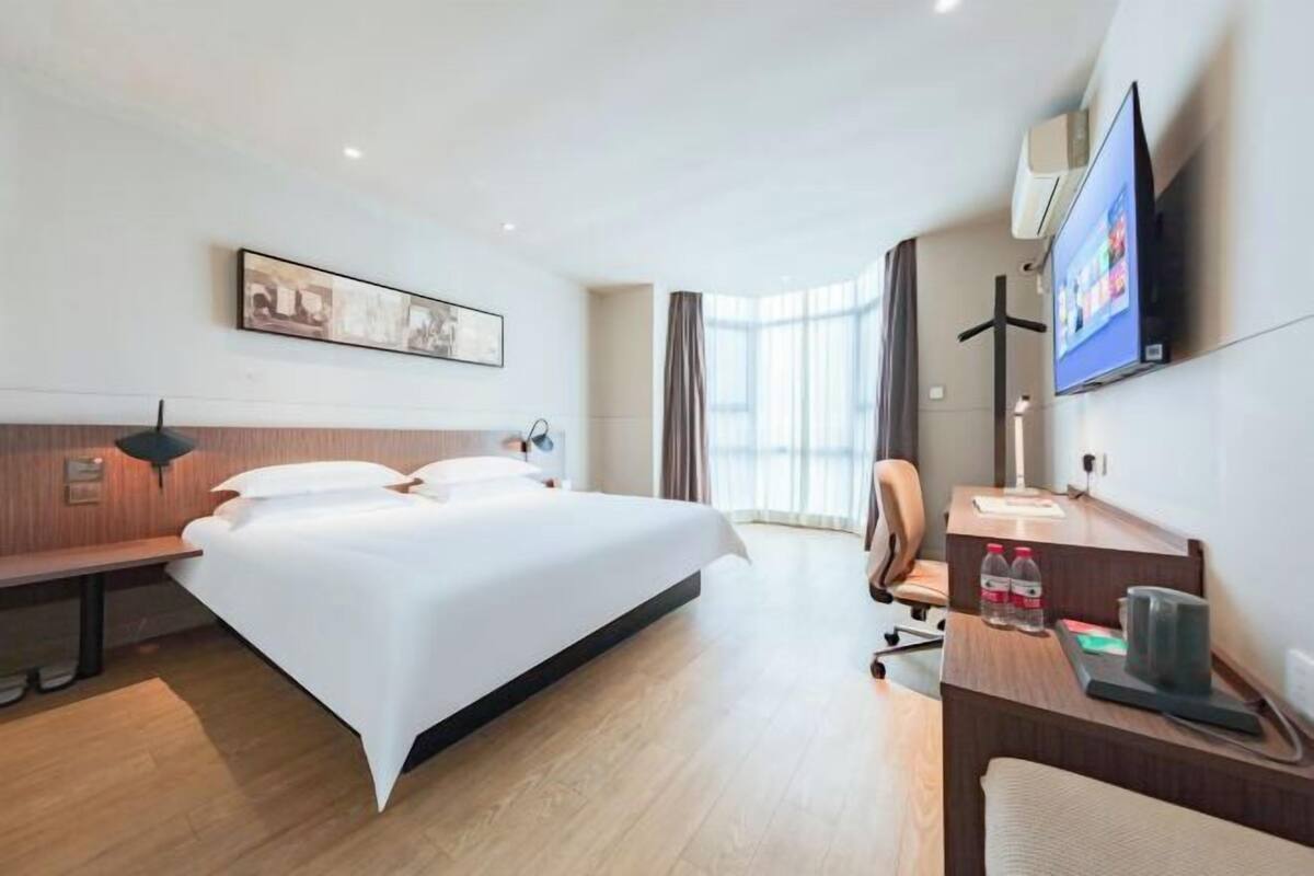 A hotel room with a bed, desk, chair, TV, and artwork on the wall.