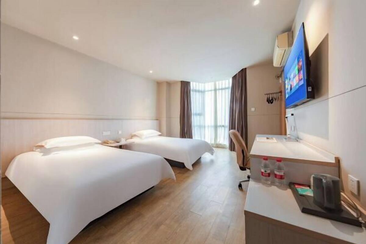 A hotel room with two beds, a desk, a TV, and a window with curtains.