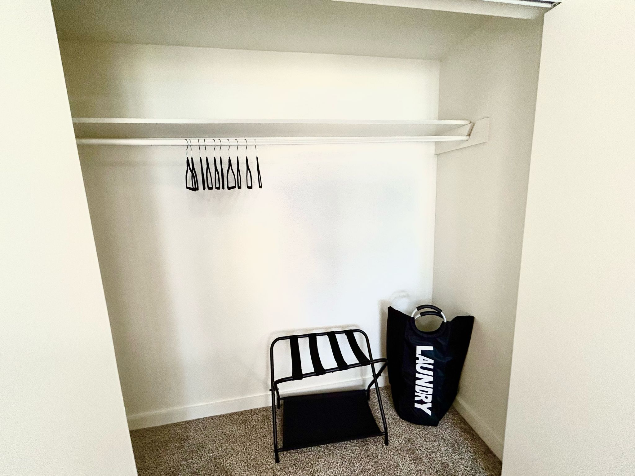 A small laundry room with a white wall, a metal drying rack, a black laundry bag, and a black and white striped chair.