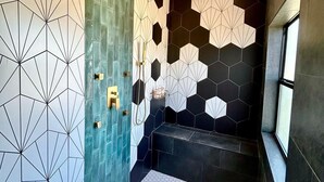 Ein modernes Badezimmer mit geometrischen Fliesenmustern, einer Duschkabine und einer Sitzbank.