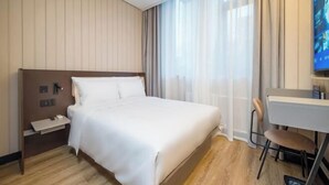 Quarto de hotel com cama, escrivaninha, cadeira, televisão e janela com cortinas.