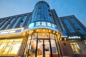 A hotel with a modern glass facade and a prominent entrance with illuminated signage. - HanTing Hotel (Beijing Shijingshan Pingguoyuan) (Beijing)