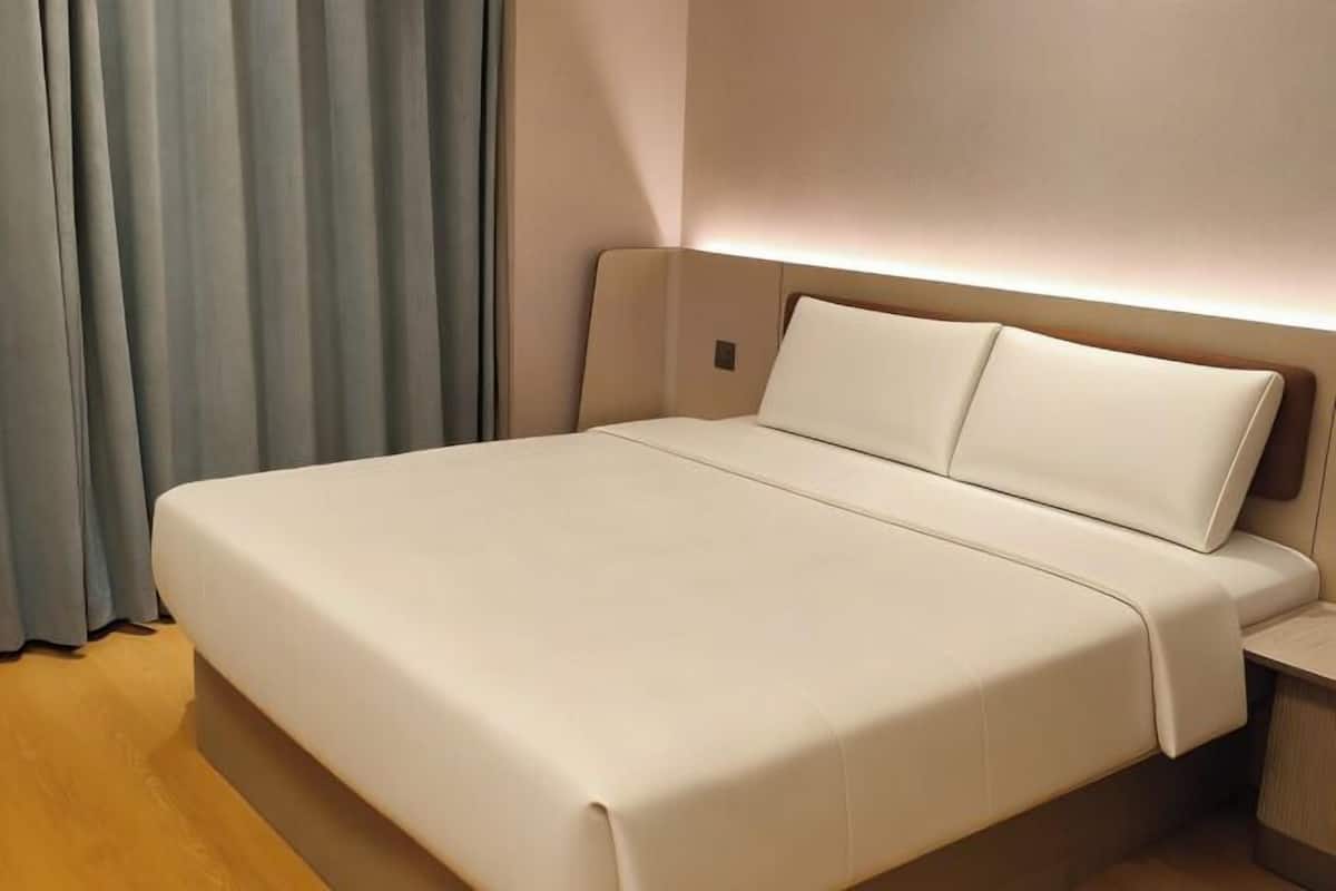 A hotel room with a large bed, a bedside table, and a curtain.