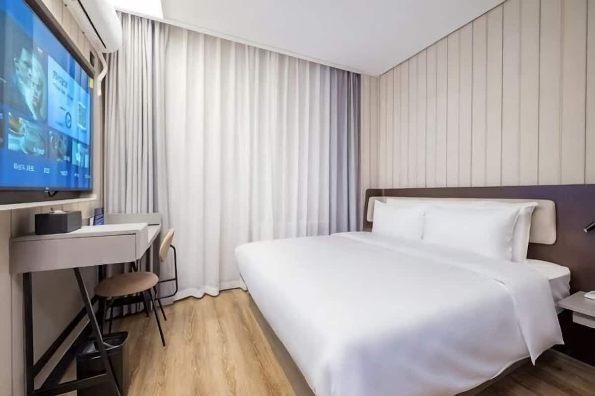 A hotel room with a bed, a desk, a chair, a TV, and a window with curtains.