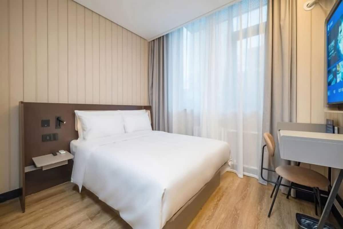 A hotel room with a bed, a desk, a chair, a TV, and a window with curtains.