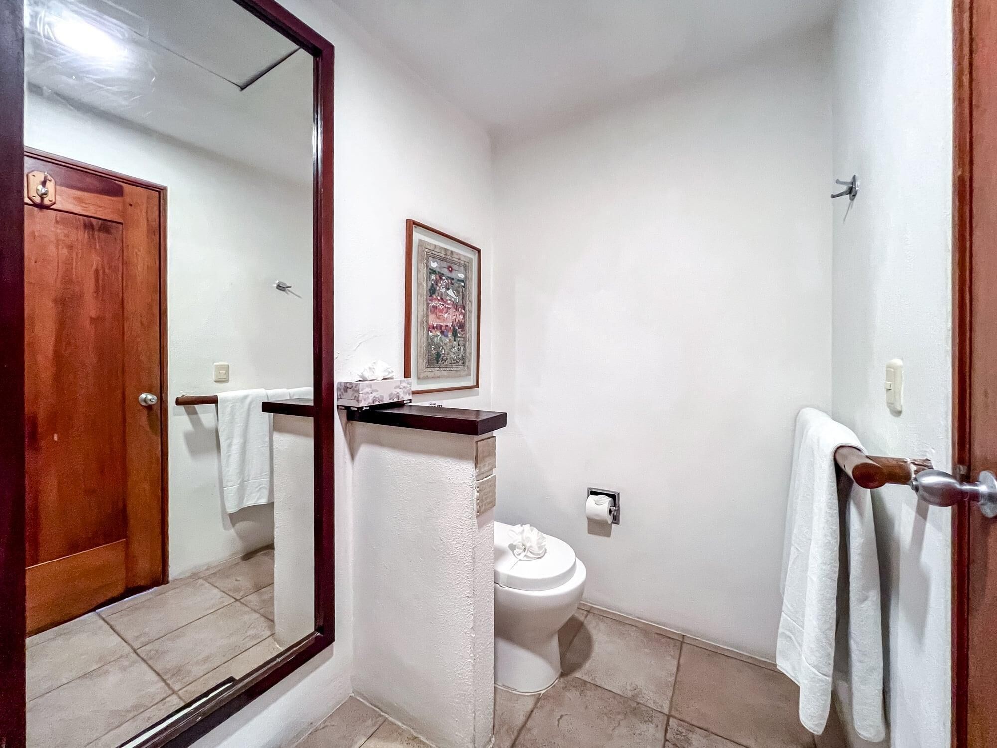 Uma casa de banho com sanita, lavatório, espelho e porta.
