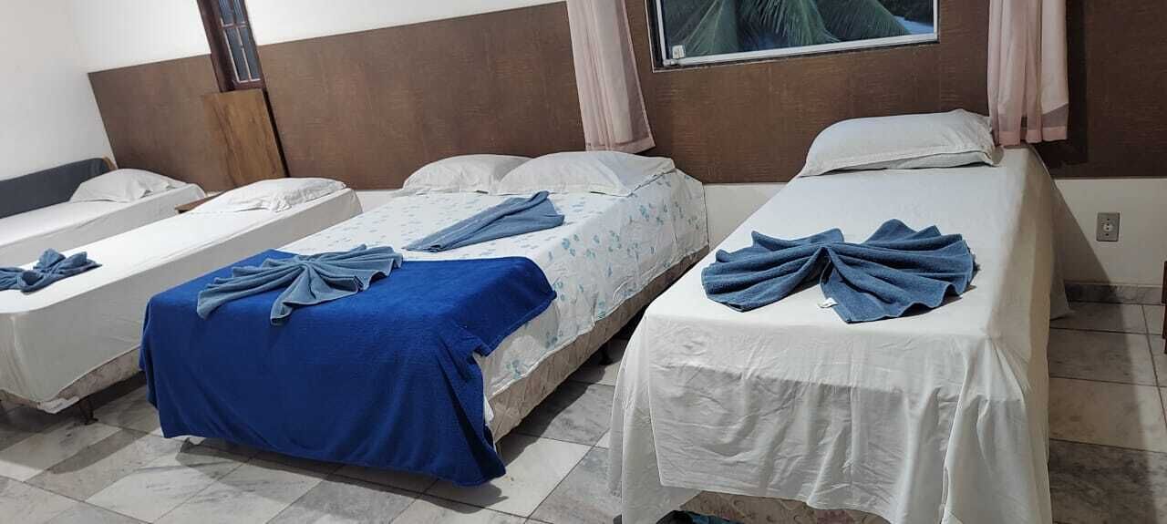 Habitación de hotel con tres camas individuales, cada una con una toalla azul y sábanas blancas.