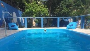A swimming pool with a blue color, surrounded by a fence and trees. - Pousada Paraiso Azul (Anchieta)